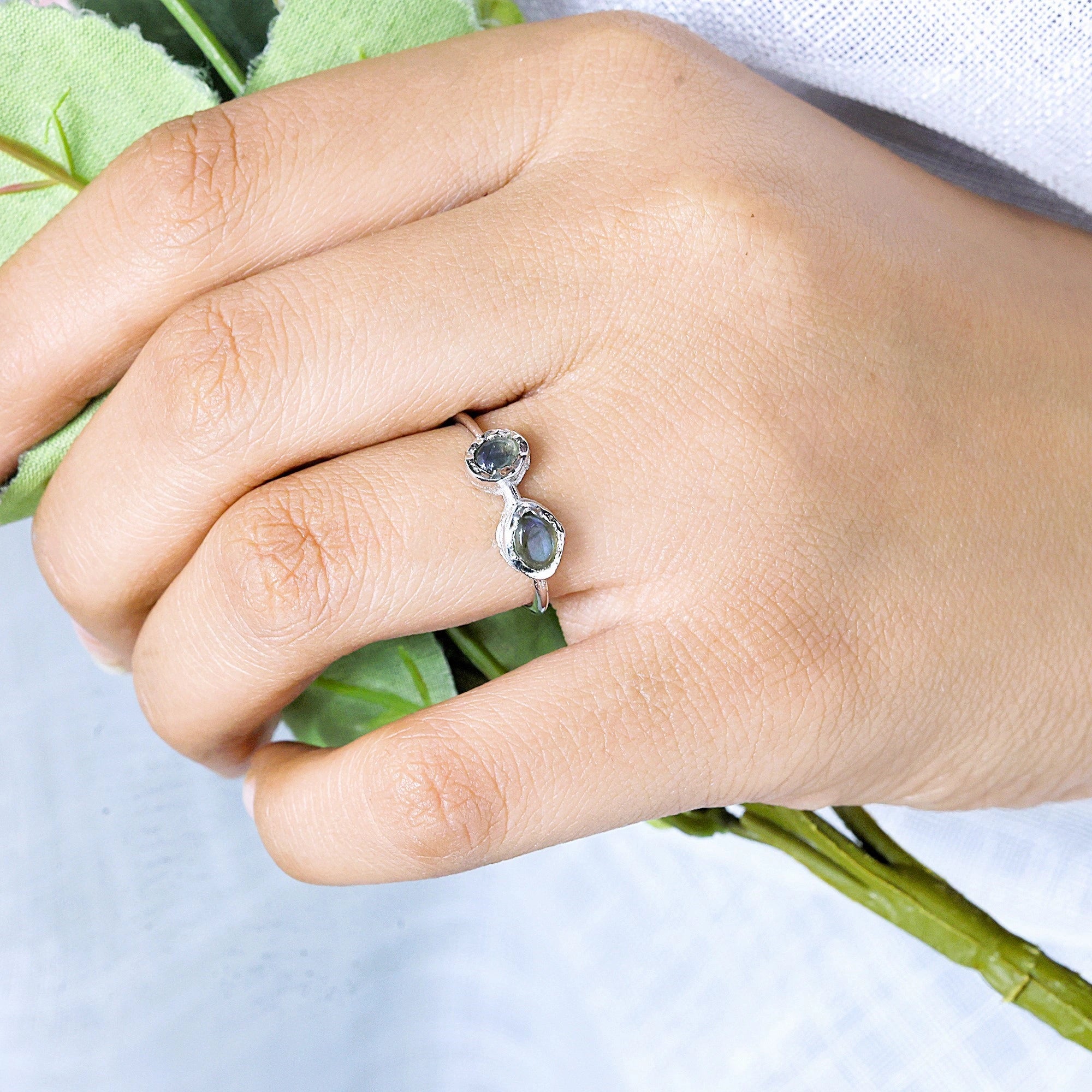 Double stone ring featuring two oval labradorite gems on a model's hand holding a stem angled view