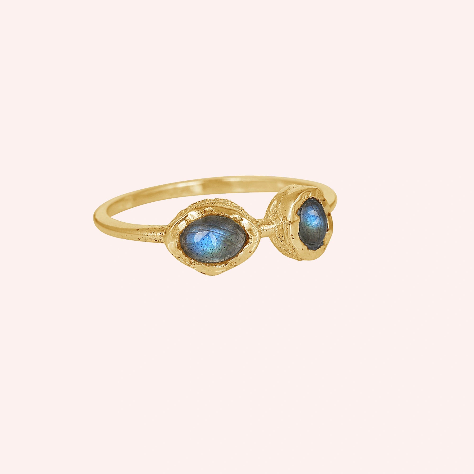 Gold plated double stone ring featuring two oval labradorite gems on a pale pink background slight right angle view
