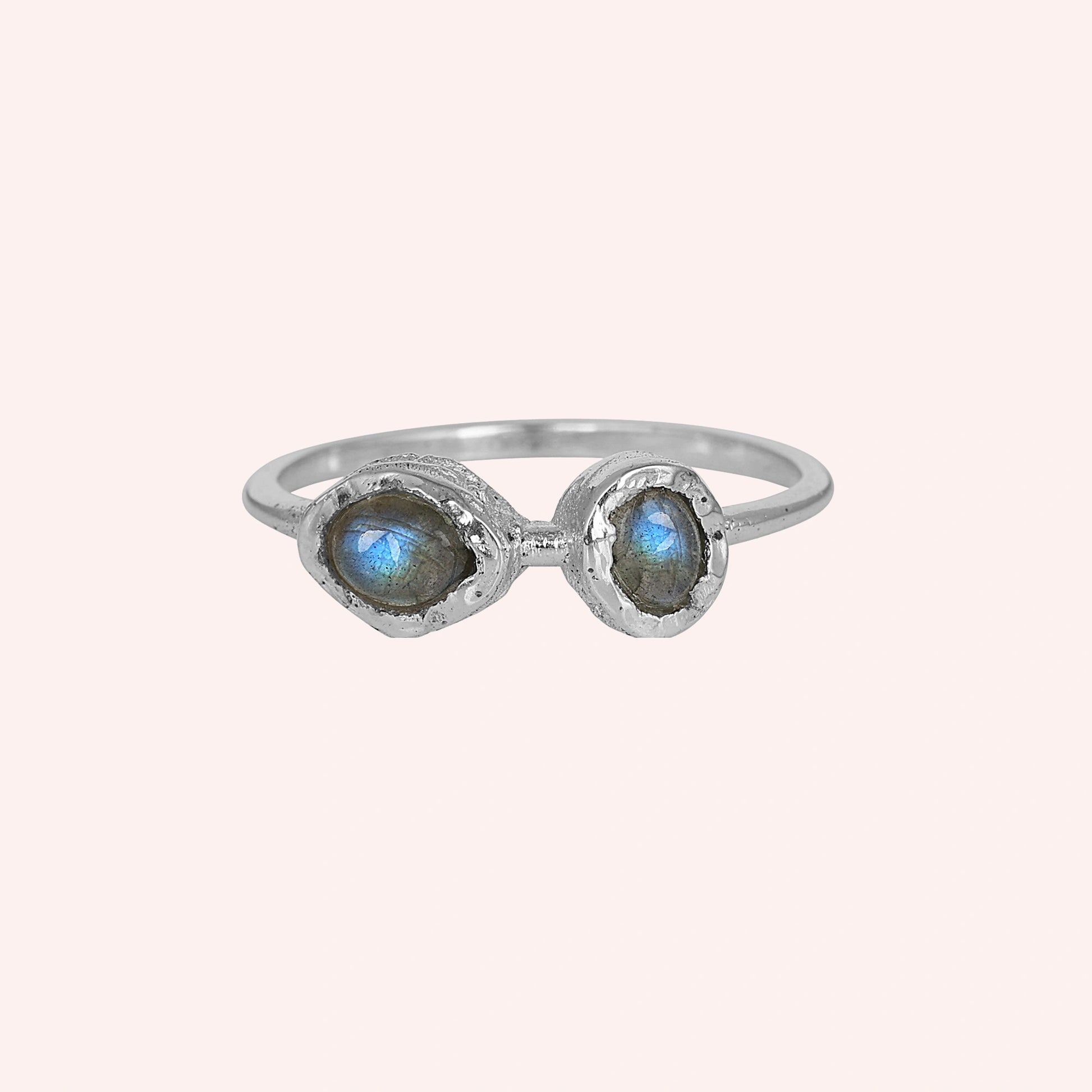 Double stone ring featuring two oval labradorite gems in rugged silver setting on a pale pink background at a straight on angle