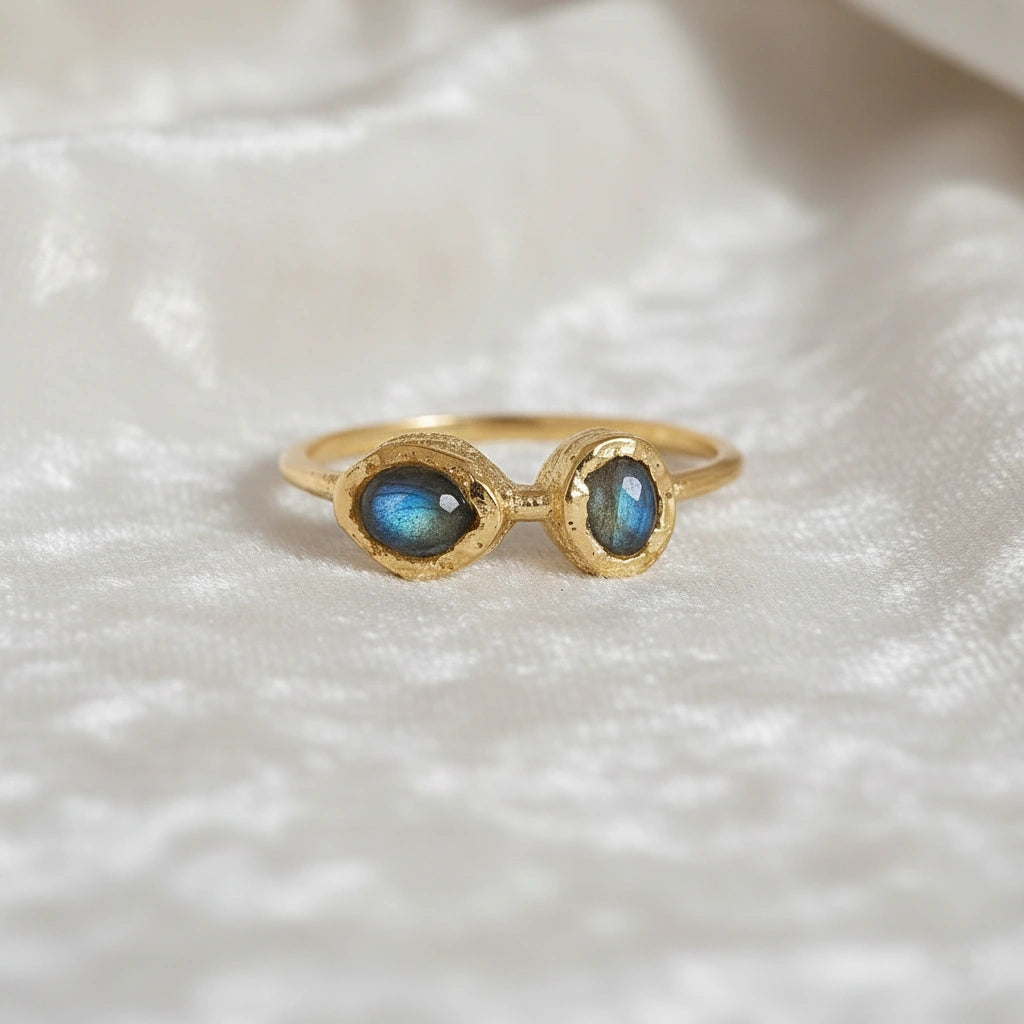 Gold plated double stone ring featuring two oval labradorite gems in rugged settings on a white cloth at a straight-on angle