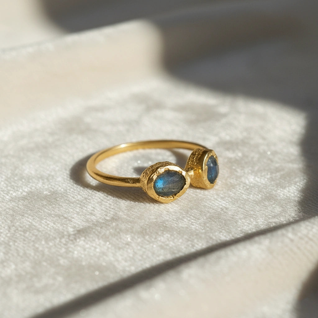 Gold plated double stone ring featuring two oval labradorite gems in rugged settings on a white cloth at a slight right angle