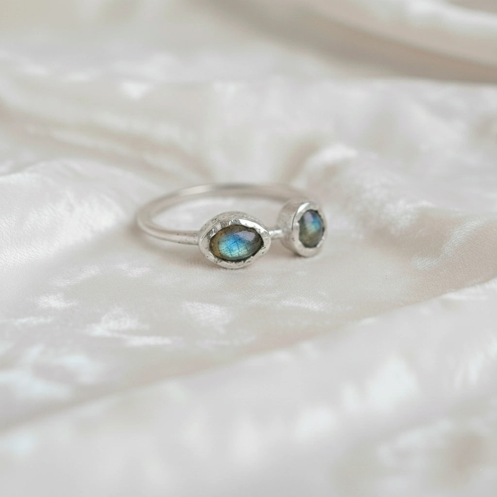 Double stone ring featuring two oval labradorite gems in rugged silver settings on a white cloth slight-right angle