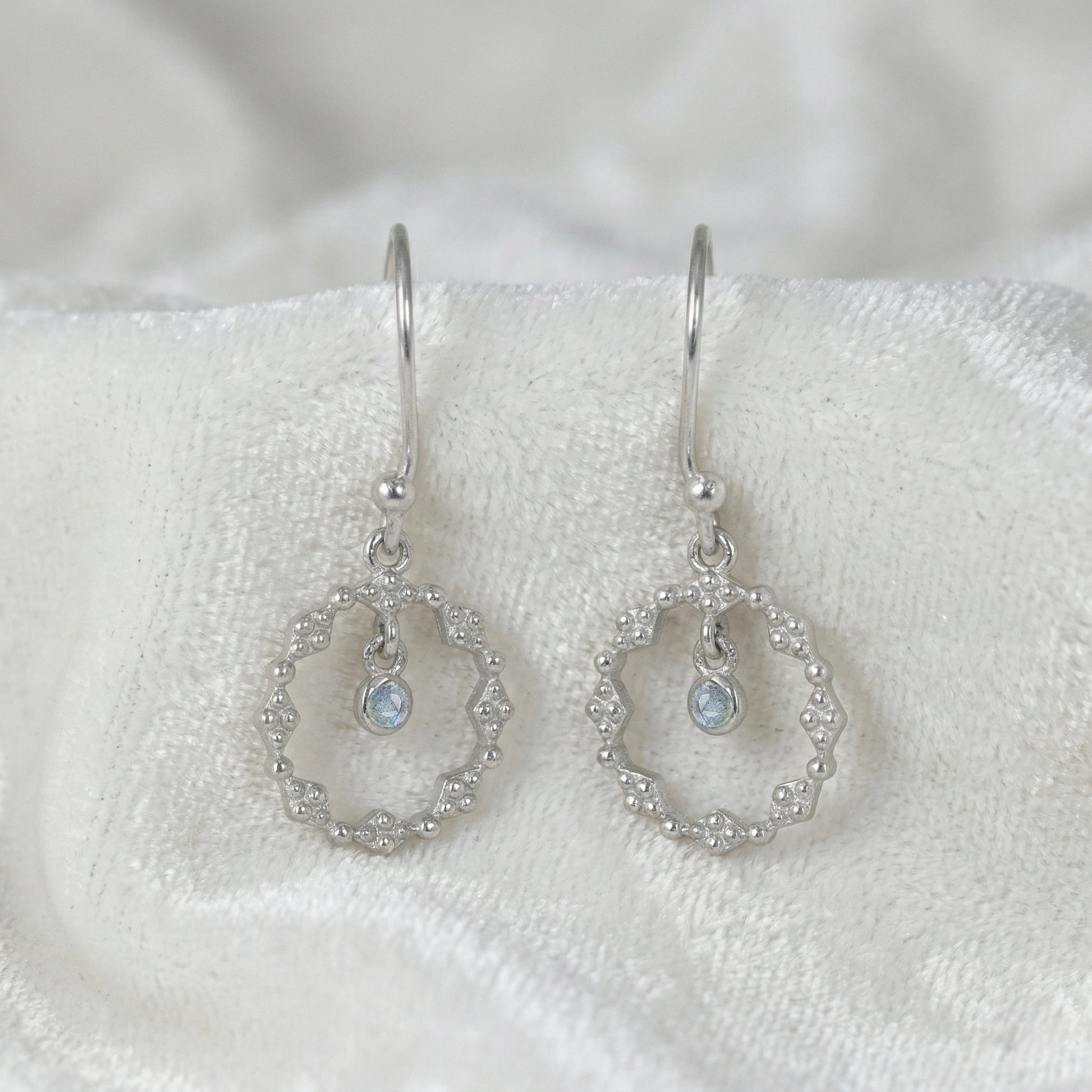 Drop_earrings_sterling_silver_with_textured_design_and_labradorite_stone_in_front_angle_on_soft_white_fabric_background