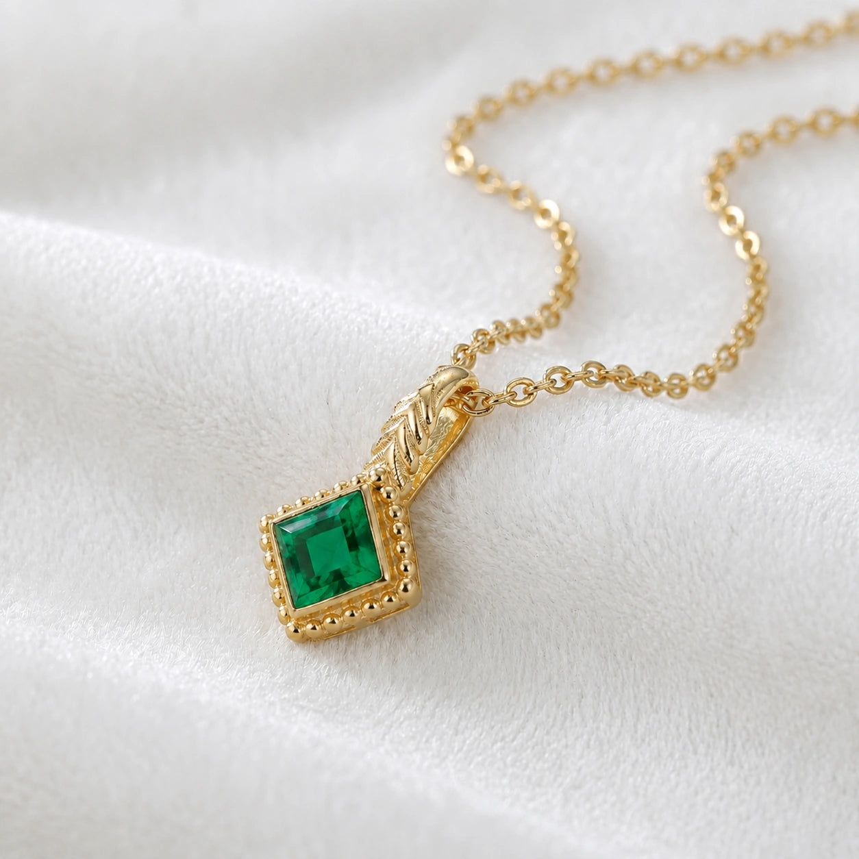 Birthstone_necklace_in_gold_plated_silver_with_square_cut_emerald_pendant_in_slighlty_angled_view_on_soft_white_fabric_background