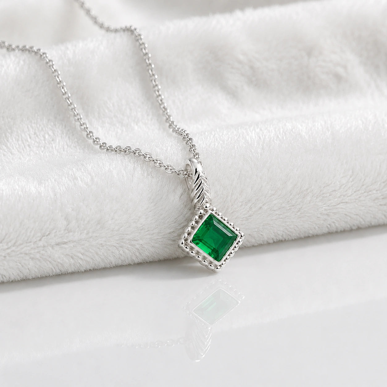 Birthstone_necklace_in_sterling_silver_with_square_cut_emerald_pendant_in_slighlty_angled_view_on_soft_white_fabric_background