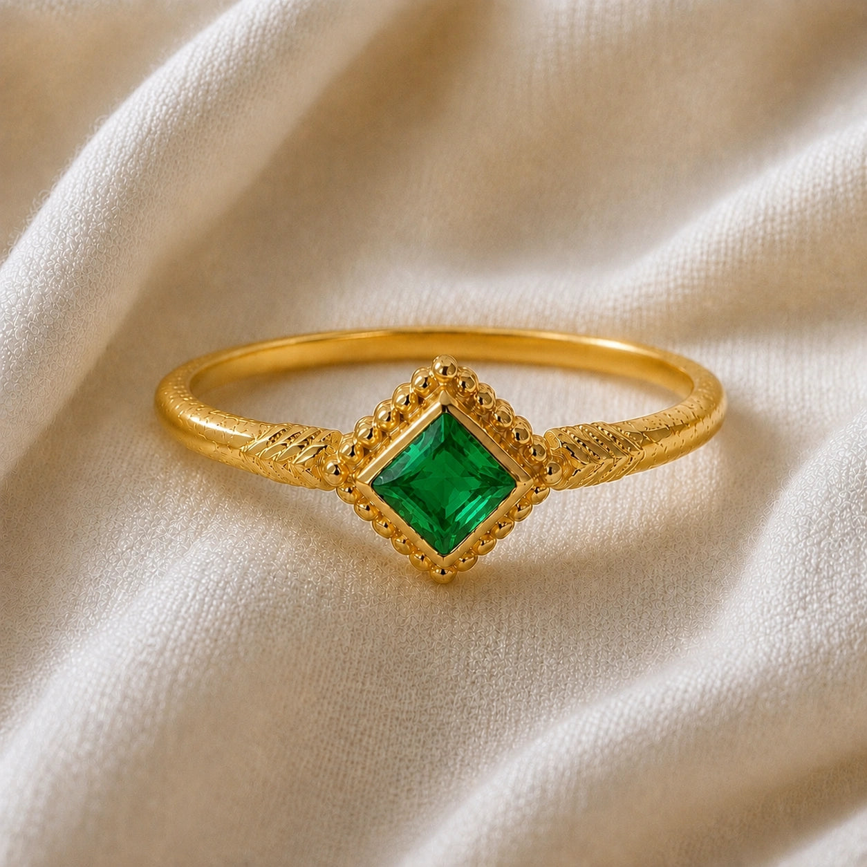 Princess_cut_ring_gold_plated_silver_with_square_emerald_and_detailed_band_front_angle_view_on_soft_fabric_background
