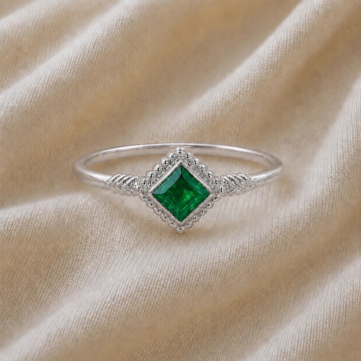 Princess_cut_ring_sterling_silver_with_square_emerald_and_detailed_band_front_angle_view_on_soft_fabric_background