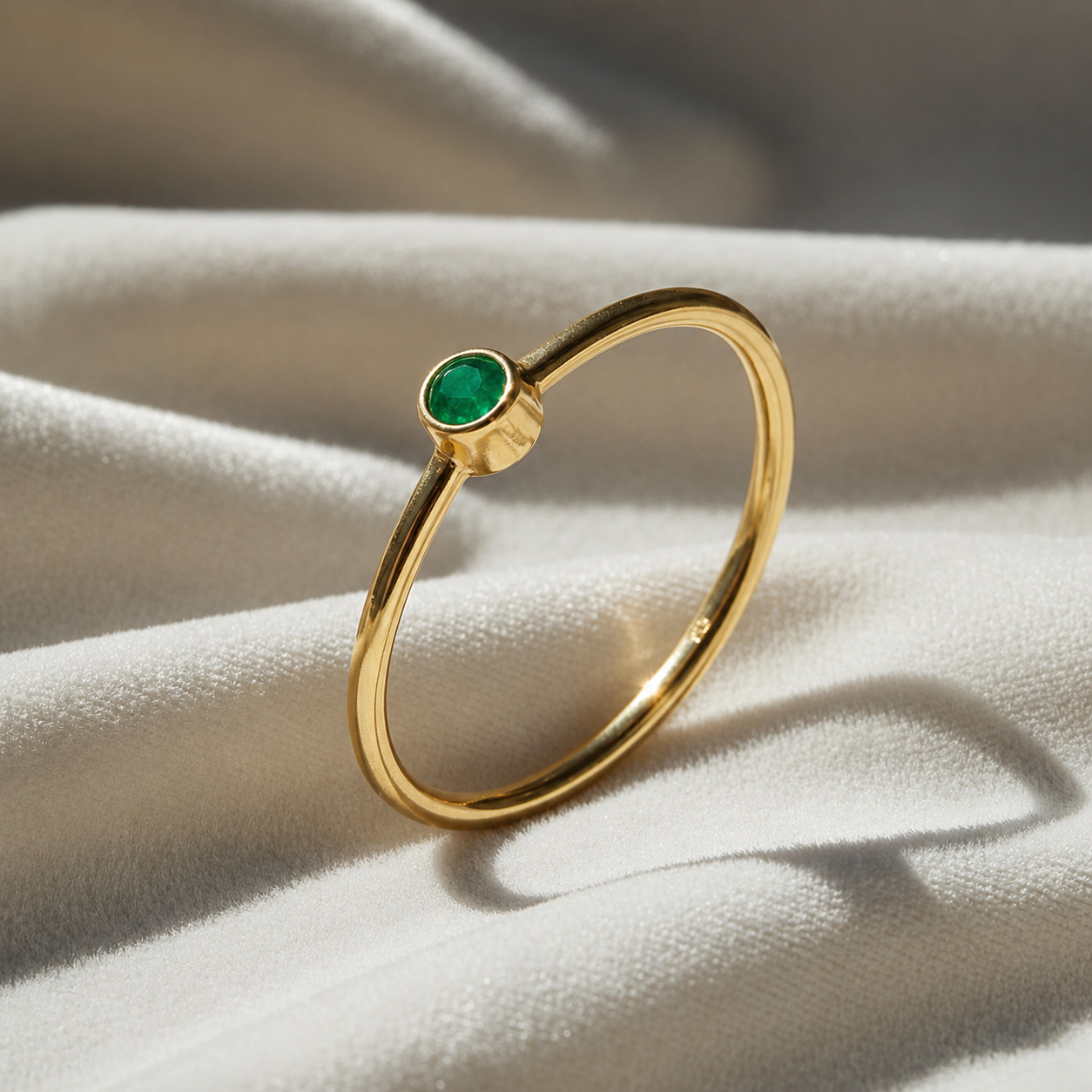 A gold plated birthstone ring featuring a emerald gemstone, styled as a delicate stacking ring on a soft white fabric background