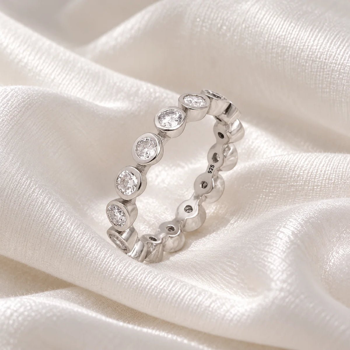 Eternity_ring_in_sterling_silver_with_CZ_stones_at_side_angle_view_on_soft_fabric_background