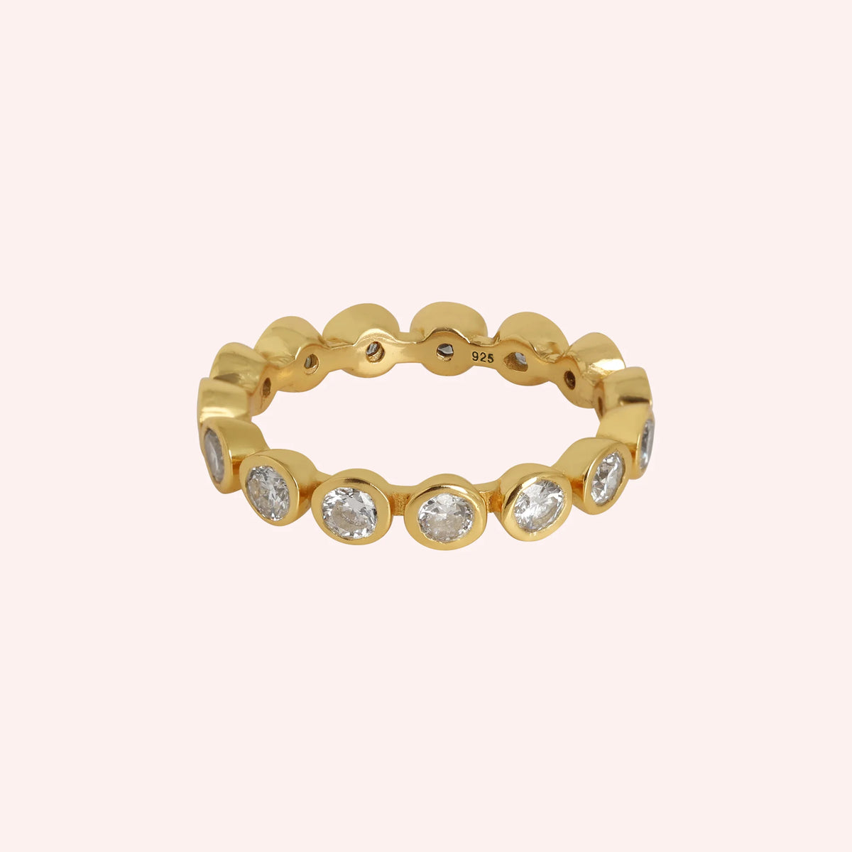 Eternity_ring_in_gold_plated_silver_with_CZ_stones_at_front_angle_view_on_solid_pink_background