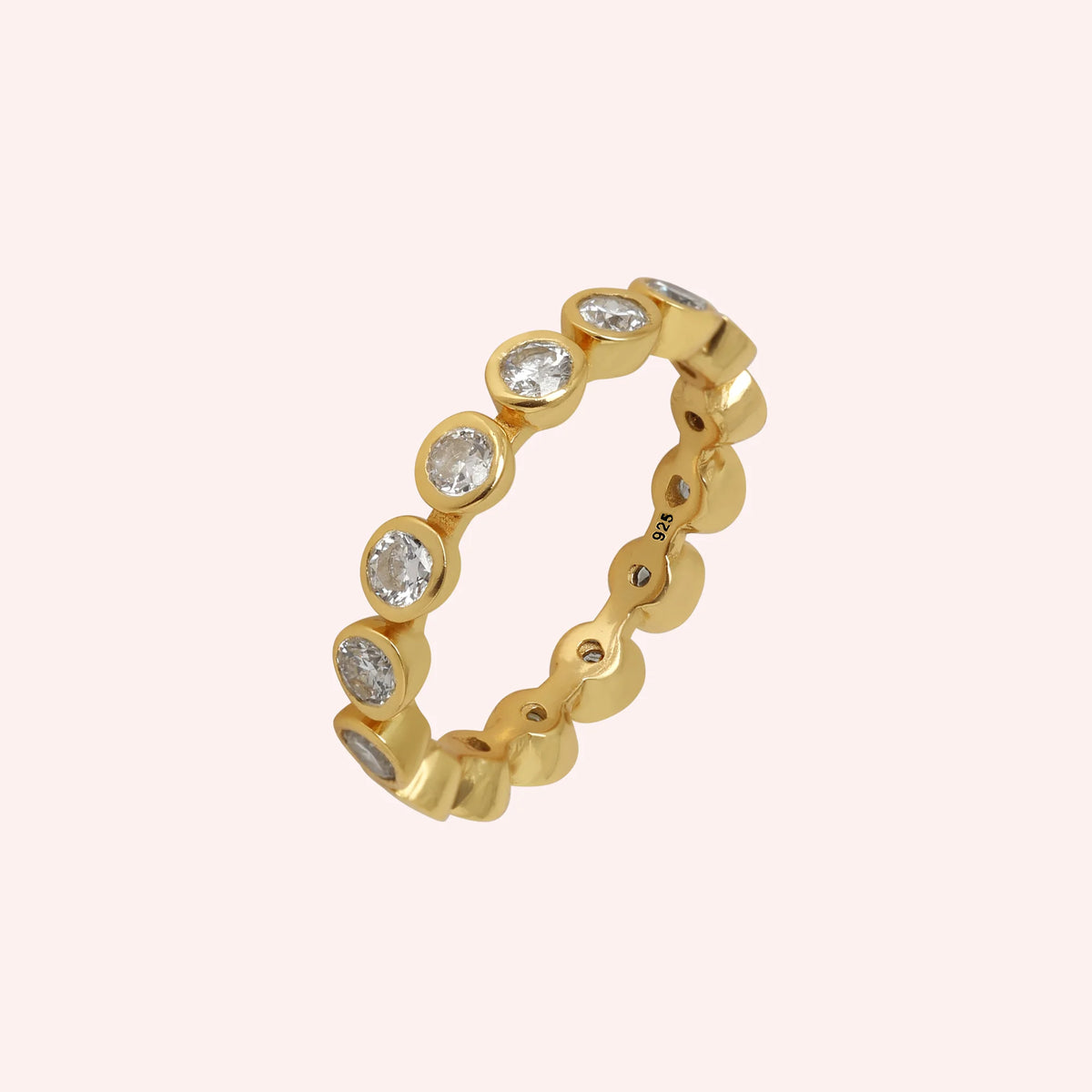 Eternity_ring_in_gold_plated_silver_with_CZ_stones_at_side_angle_view_on_solid_pink_background