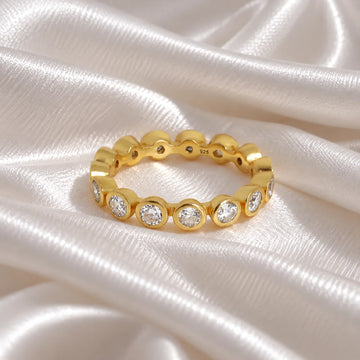 Eternity_ring_in_gold_plated_silver_with_CZ_stones_at_front_angle_view_on_soft_fabric_background