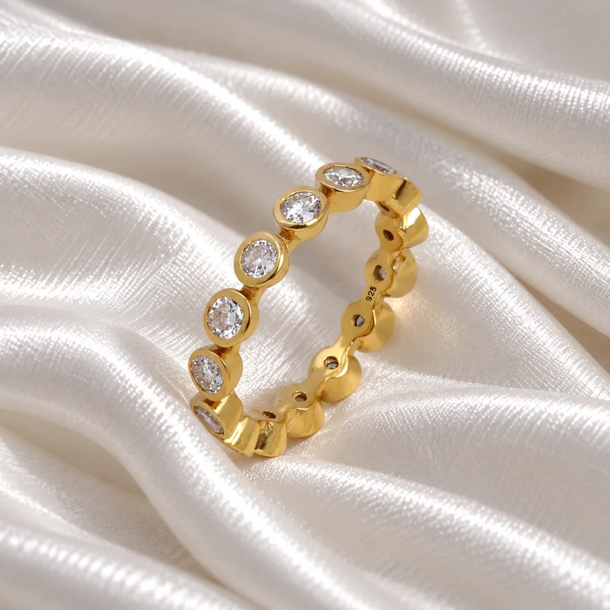 Eternity_ring_in_gold_plated_silver_with_CZ_stones_at_side_angle_view_on_soft_fabric_background