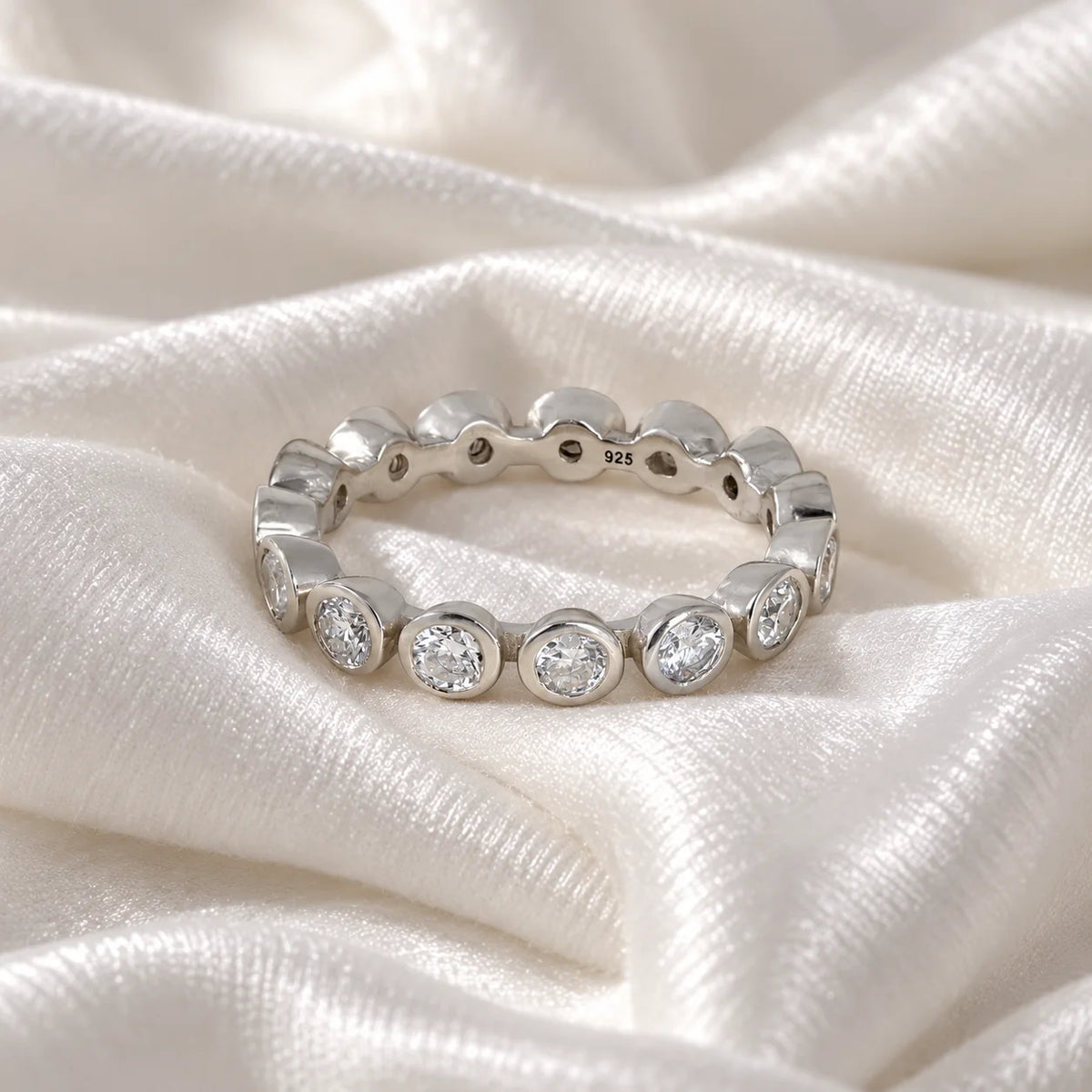 Eternity_ring_in_sterling_silver_with_CZ_stones_at_front_angle_view_on_soft_fabric_background