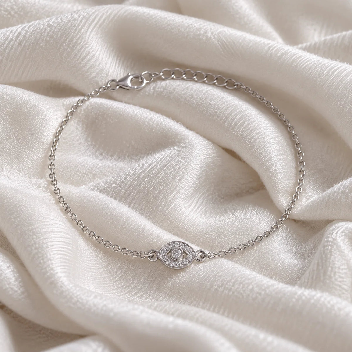 Evil_eye_bracelet_in_sterling_silver_with_CZ_stones_at_front_angle_view_on_soft_fabric_background