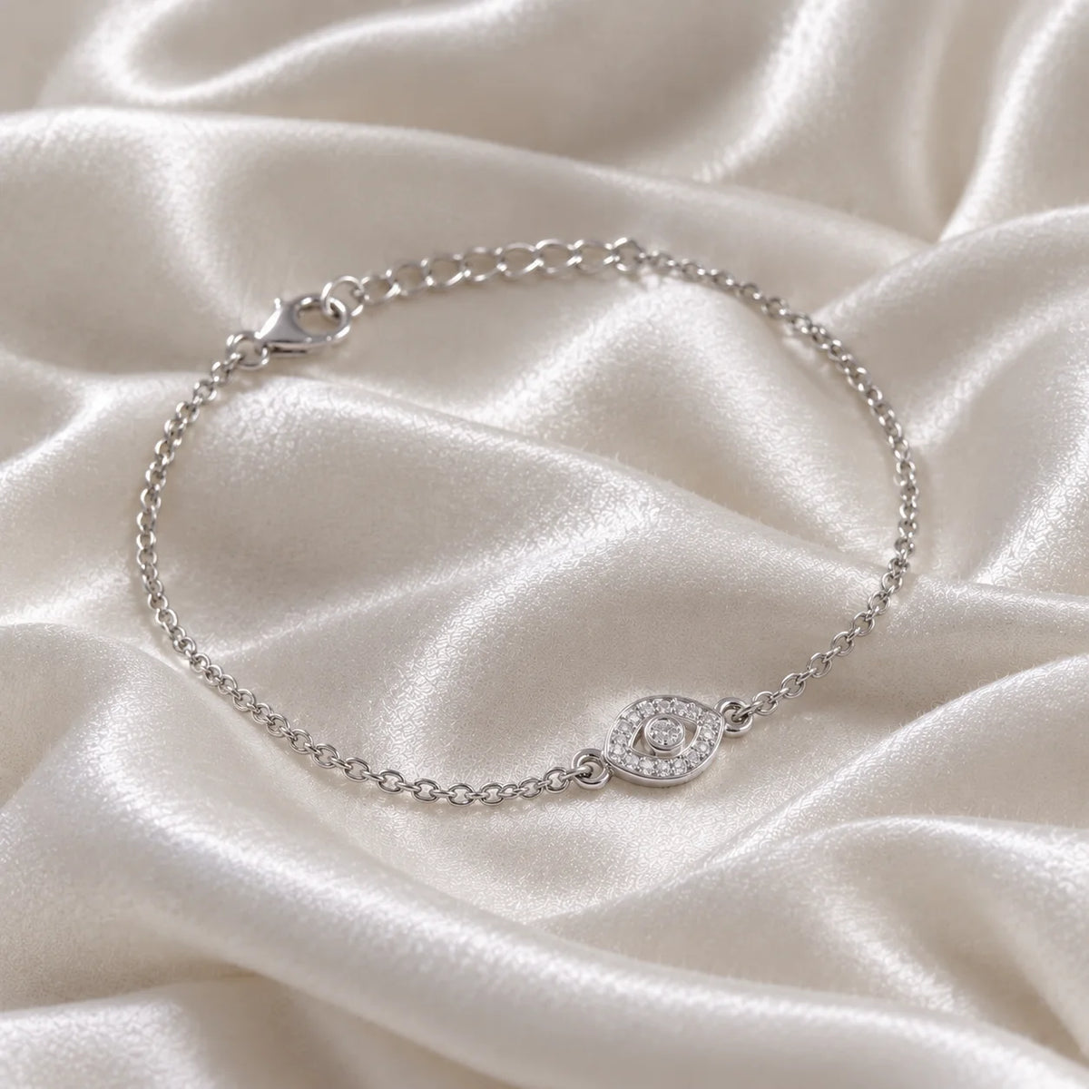 Evil_eye_bracelet_in_sterling_silver_with_CZ_stones_at_side_angle_view_on_soft_fabric_background
