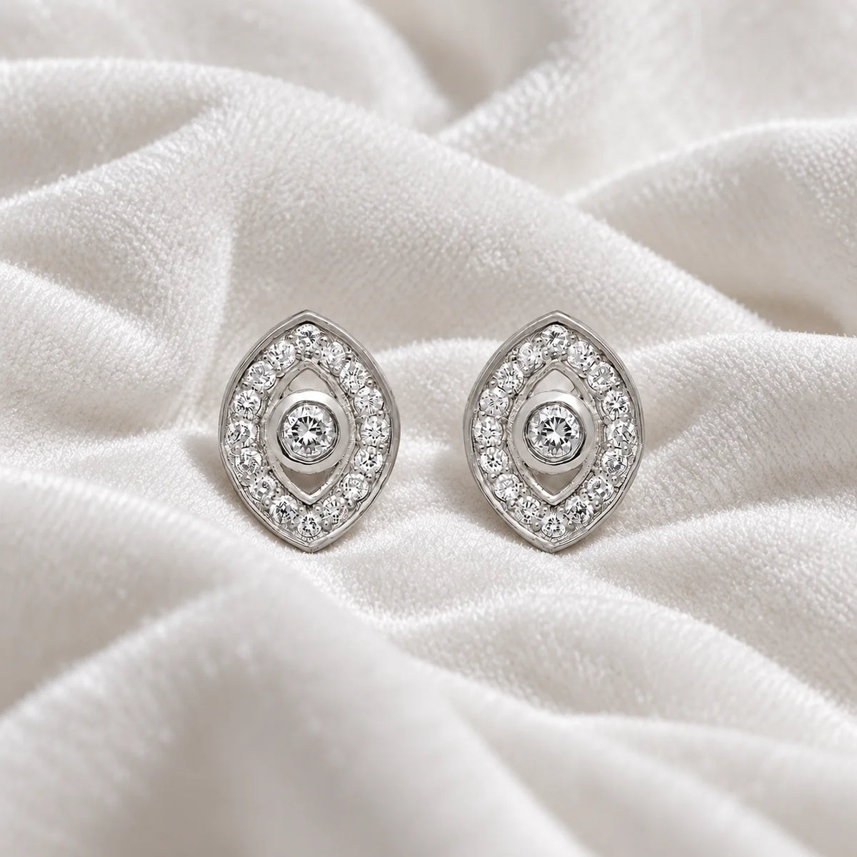 Evil_eye_earrings_in_sterling_silver_with_CZ_stones_at_front_angle_view_on_soft_fabric_background