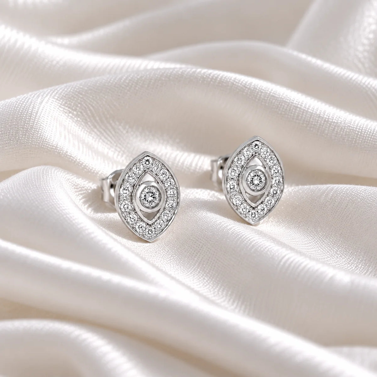Evil_eye_earrings_in_sterling_silver_with_lab_grown_diamonds_at_front_angle_view_on_soft_fabric_background