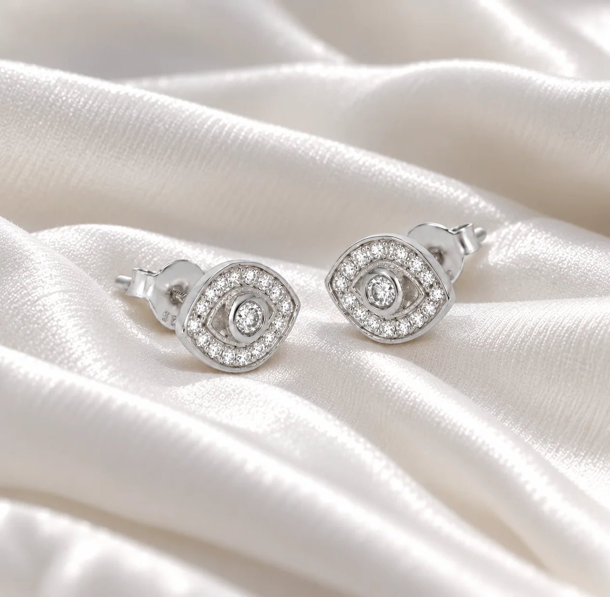 Evil_eye_earrings_in_sterling_silver_with_lab_grown_diamonds_at_slight_angle_view_on_soft_fabric_background