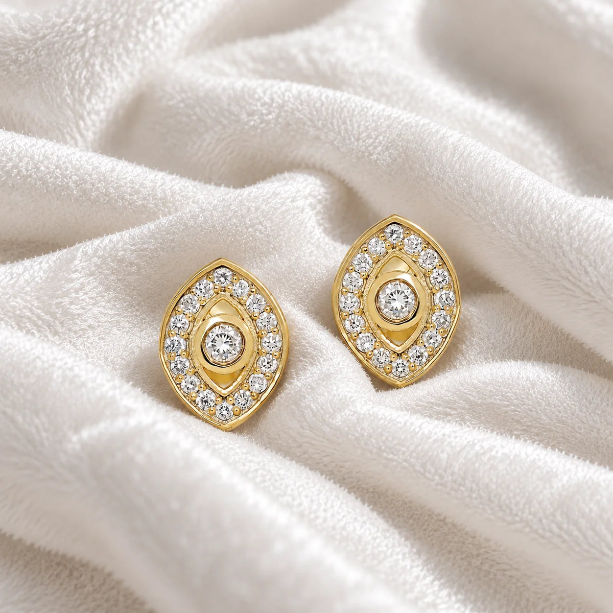 Evil_eye_earrings_in_gold_plated_silver_with_CZ_stones_at_front_angle_view_on_soft_fabric_background
