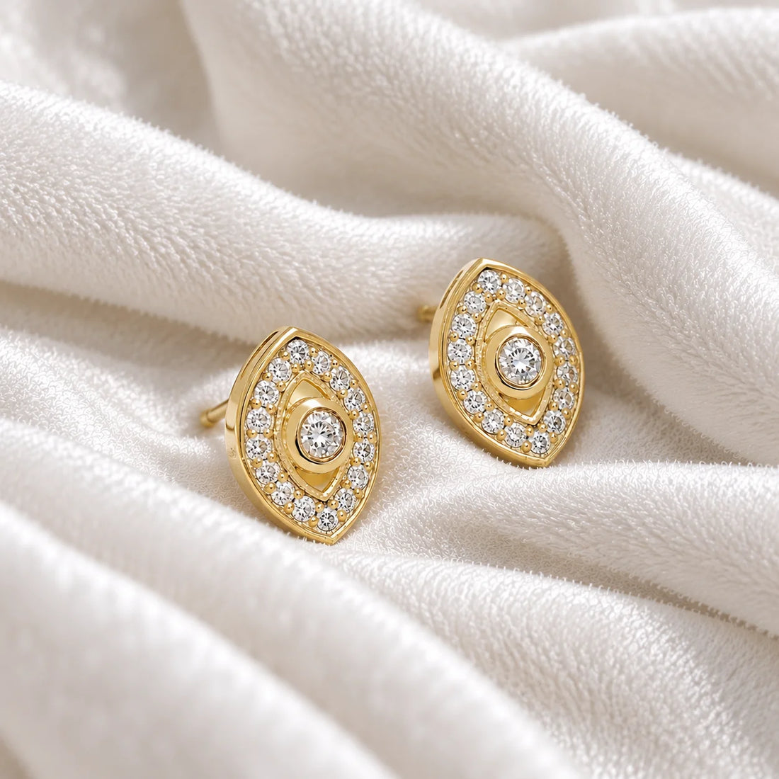 Evil_eye_earrings_in_gold_plated_silver_with_CZ_stones_at_side_angle_view_on_soft_fabric_background