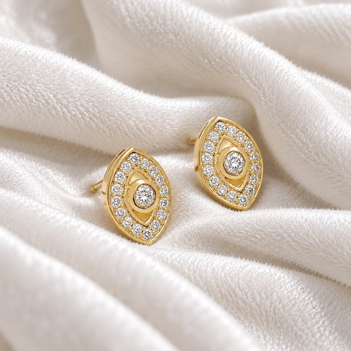 Evil_eye_earrings_in_gold_plated_silver_with_CZ_stones_at_side_angle_view_on_soft_fabric_background