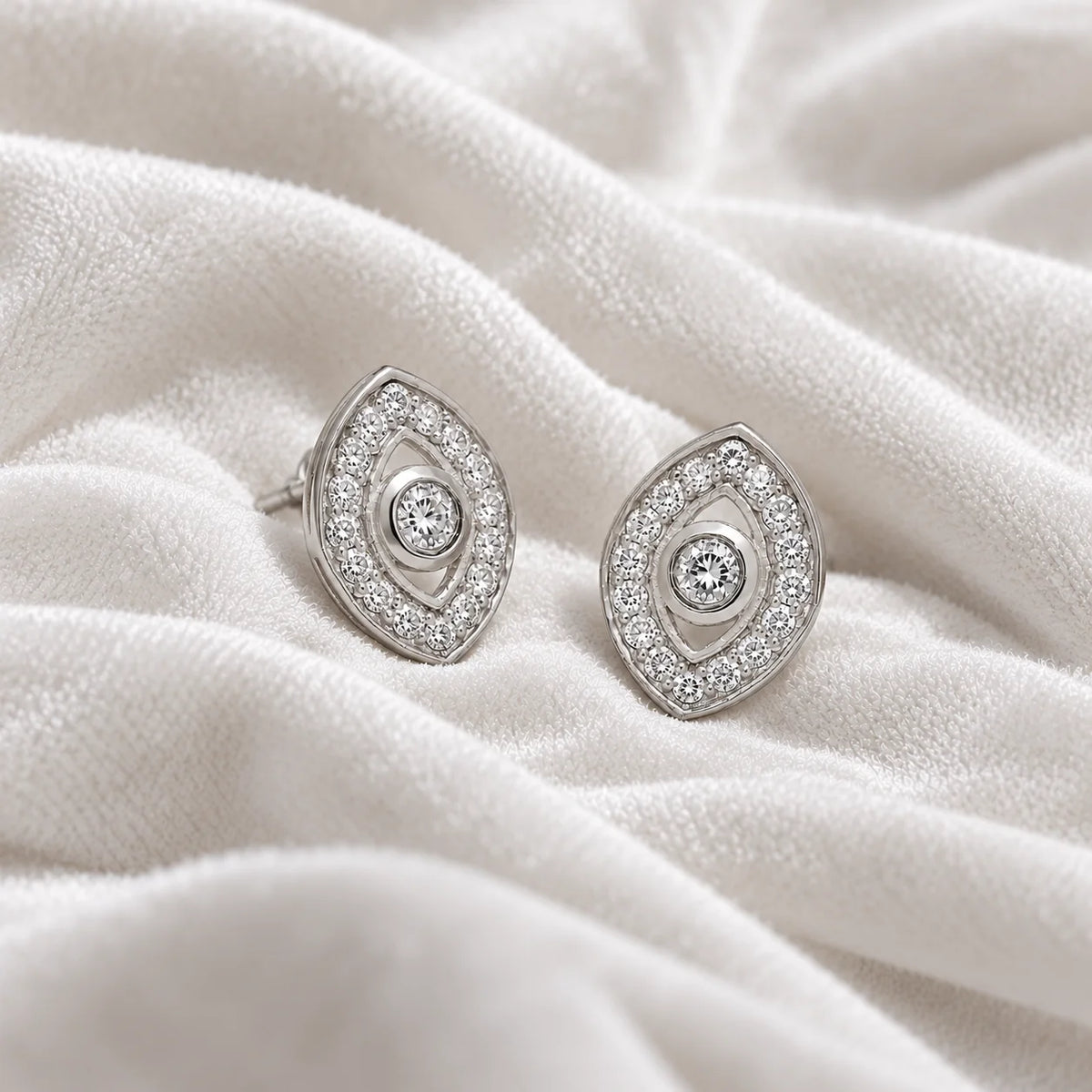 Evil_eye_earrings_in_sterling_silver_with_CZ_stones_at_side_angle_view_on_soft_fabric_background