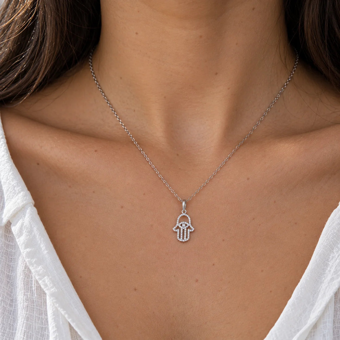 Evil_eye_necklace_in_gold_plated_silver_with_hamsa_hand_design_at_front_angle_view_on_soft_fabric_background