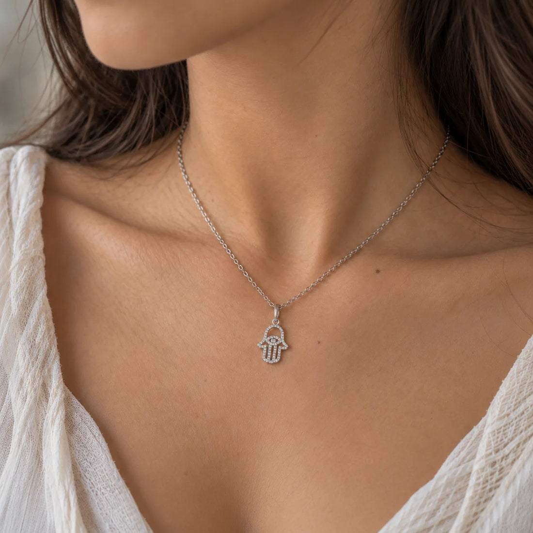 Evil_eye_necklace_in_gold_plated_silver_with_hamsa_hand_design_with_CZ_stones_at_side_angle_view_on_soft_fabric_background