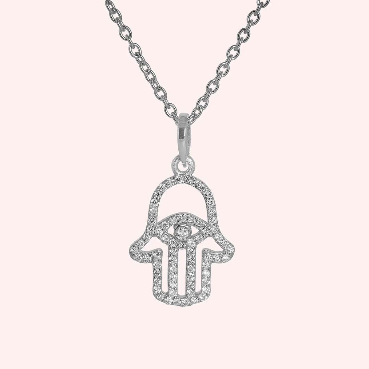 Evil_eye_necklace_in_sterling_silver_with_hamsa_hand_design_with_CZ_stones_at_front_angle_view_on_solid_pink_background