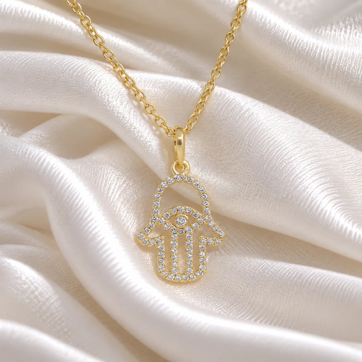 Evil_eye_necklace_in_gold_plated_silver_with_hamsa_hand_design_at_front_angle_view_on_soft_fabric_background