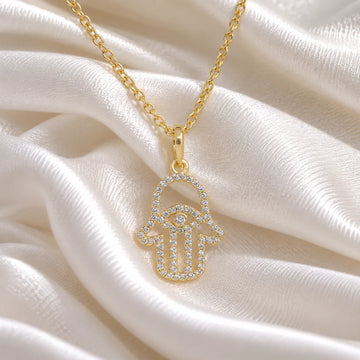 Evil_eye_necklace_in_gold_plated_silver_with_hamsa_hand_design_at_front_angle_view_on_soft_fabric_background
