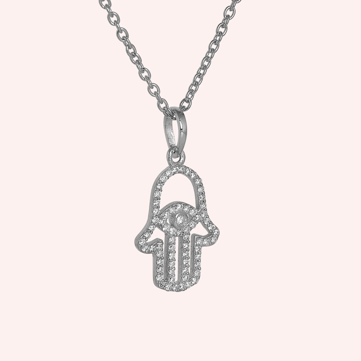 Evil_eye_necklace_in_sterling_silver_with_hamsa_hand_design_with_CZ_stones_at_side_angle_view_on_solid_pink_background