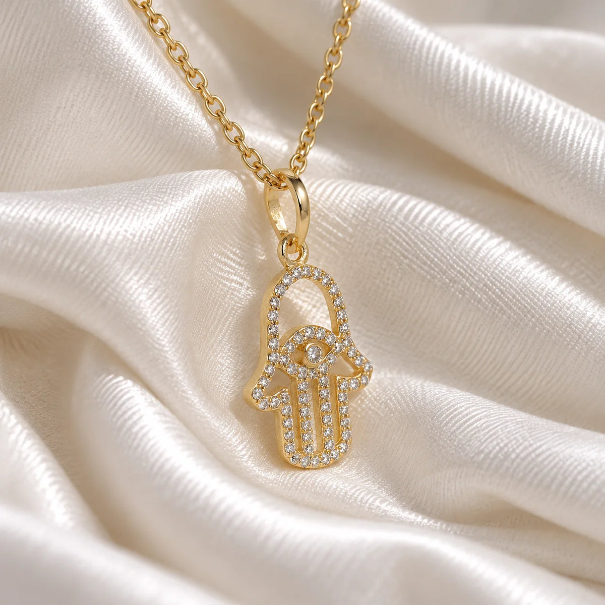Evil_eye_necklace_in_gold_plated_silver_with_hamsa_hand_design_at_slight_angle_view_on_soft_fabric_background