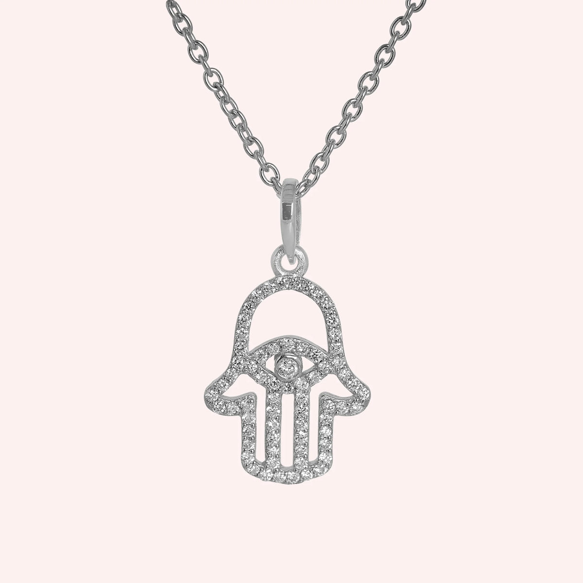 Evil_eye_necklace_in_sterling_silver_with_hamsa_hand_design_at_front_angle_view_on_solid_pink_background