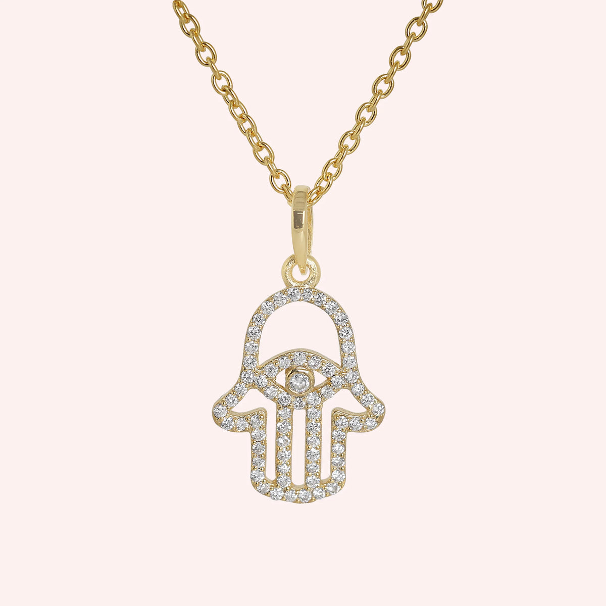 Evil_eye_necklace_in_gold_plated_silver_with_hamsa_hand_design_with_CZ_stones_at_front_angle_view_on_solid_pink_background