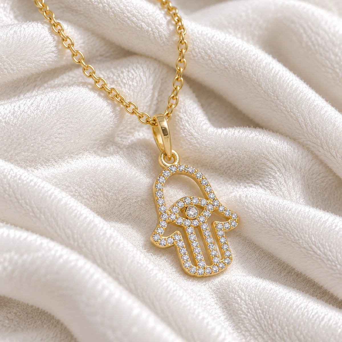 Evil_eye_necklace_in_gold_plated_silver_with_hamsa_hand_design_with_CZ_stones_at_side_angle_view_on_soft_fabric_background