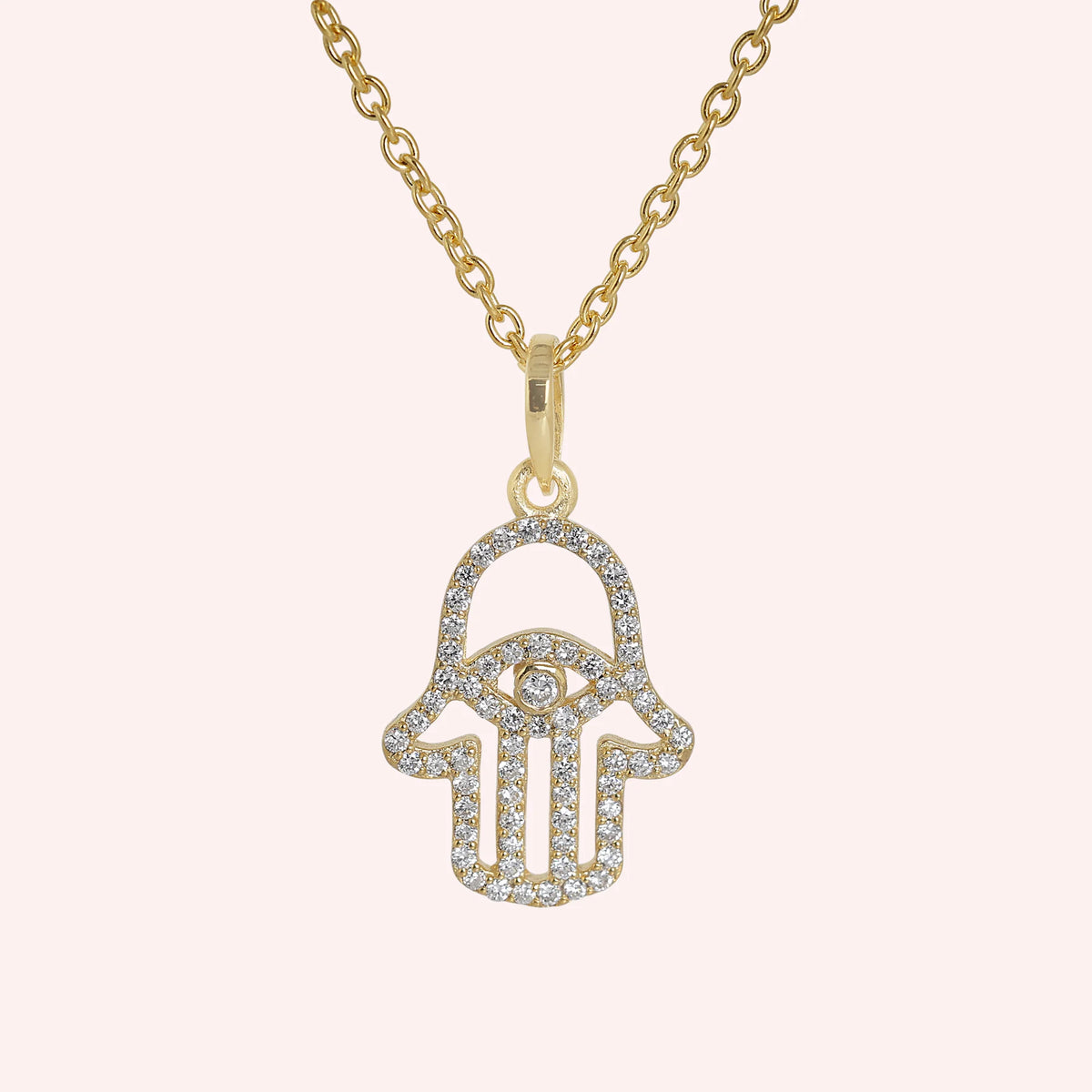 Evil_eye_necklace_in_gold_plated_silver_with_hamsa_hand_design_at_front_angle_view_on_solid_pink_background