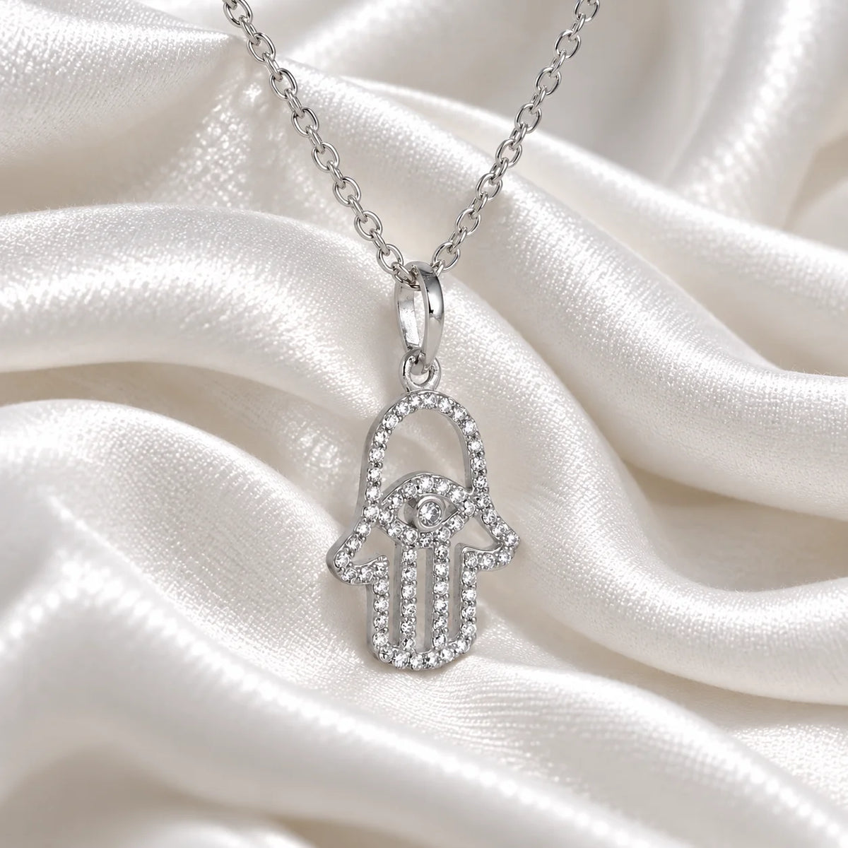 Evil_eye_necklace_in_sterling_silver_with_hamsa_hand_design_at_slight_angle_view_on_soft_fabric_background