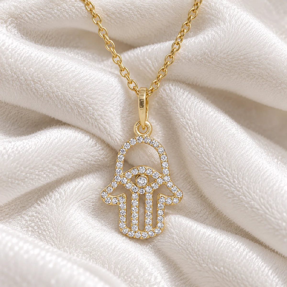 Evil_eye_necklace_in_gold_plated_silver_with_hamsa_hand_design_with_CZ_stones_at_front_angle_view_on_soft_fabric_background