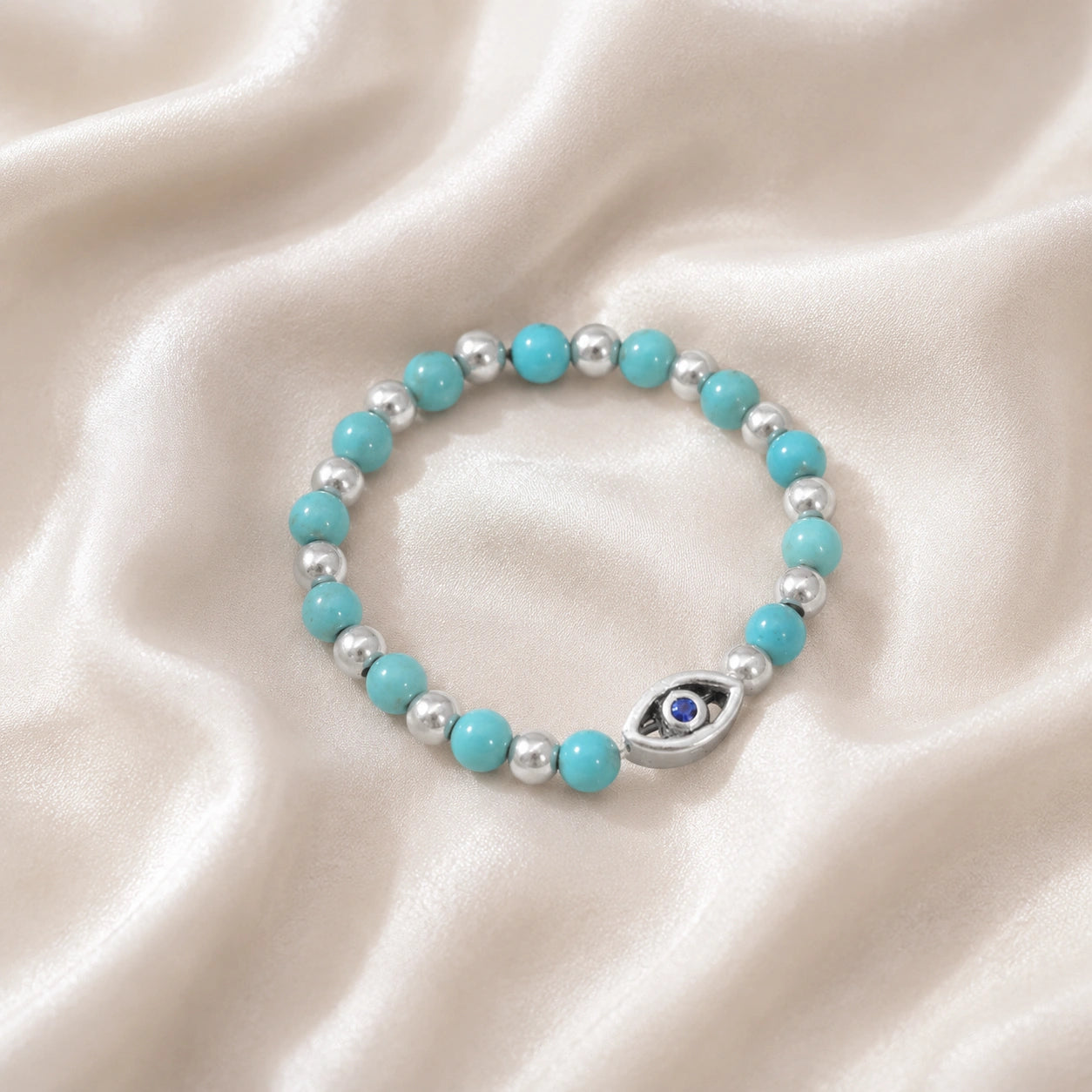 Evil_eye_ring_featuring_turquoise_and_sterling_silver_beads_with_blue_iolite_in_slightly_angled_on_soft_fabric_background