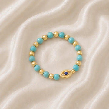 Evil_eye_ring_featuring_turquoise_and_gold_plated_silver_beads_with_blue_iolite_in_slightly_angled_on_soft_fabric_background