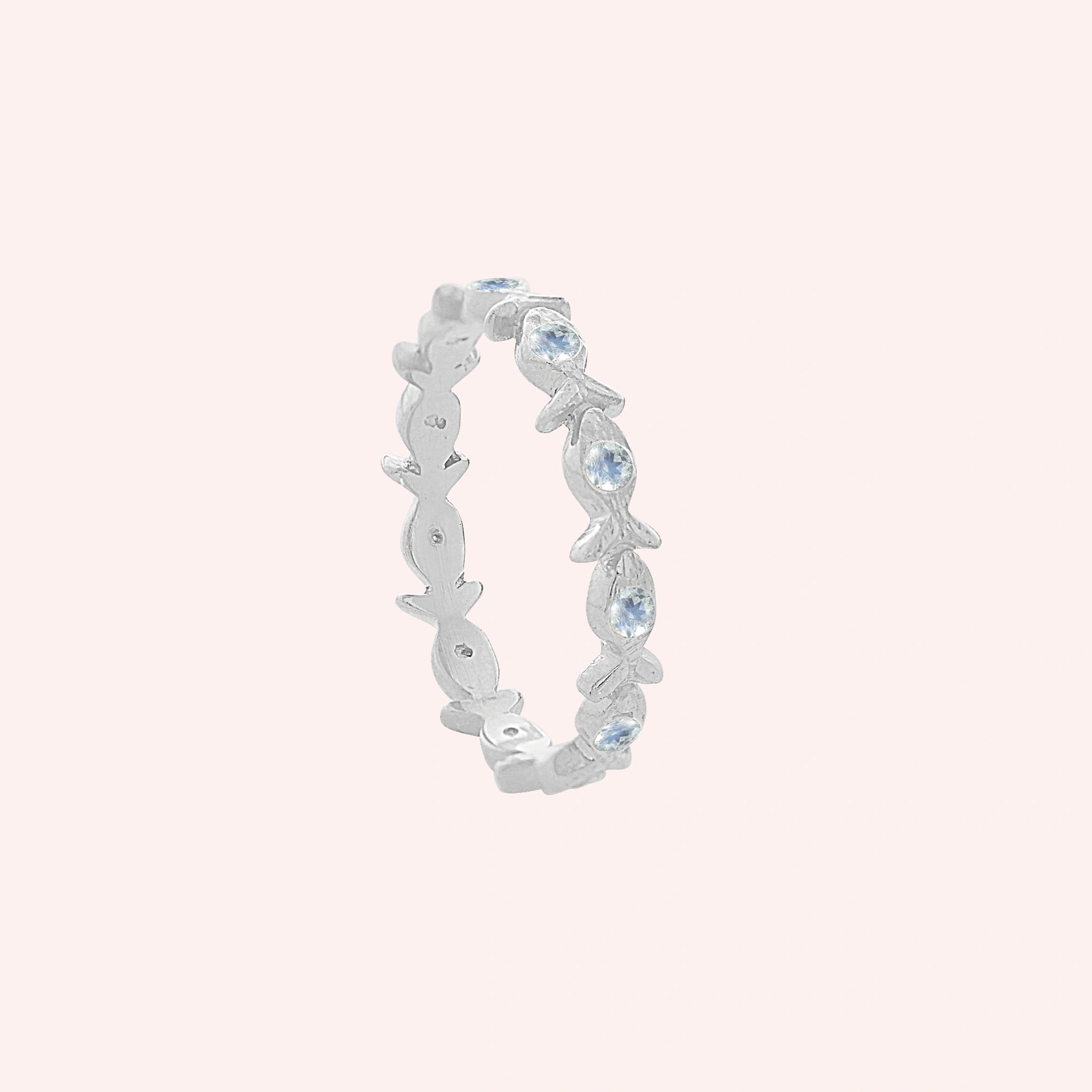 Fish_ring_sterling_silver_moonstone_eternity_band_in_side_angle_view_on_solid_pink_background