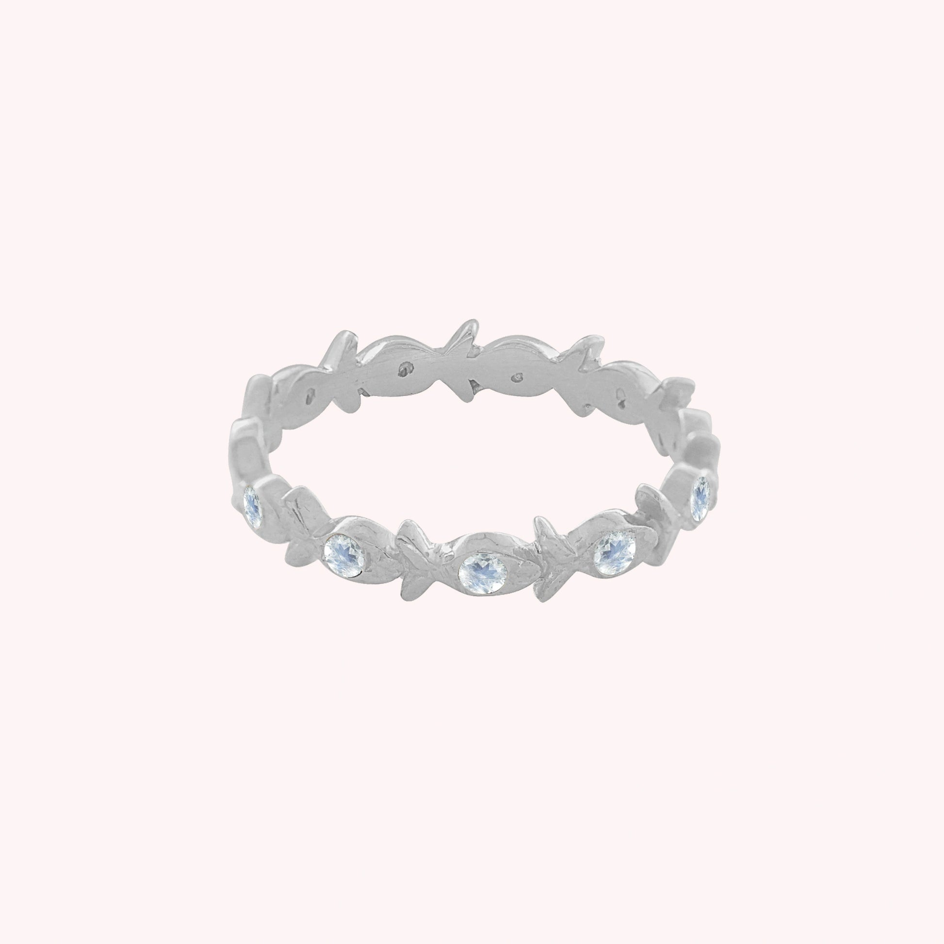 Fish_ring_sterling_silver_moonstone_eternity_band_in_front_angle_view_on_solid_pink_background