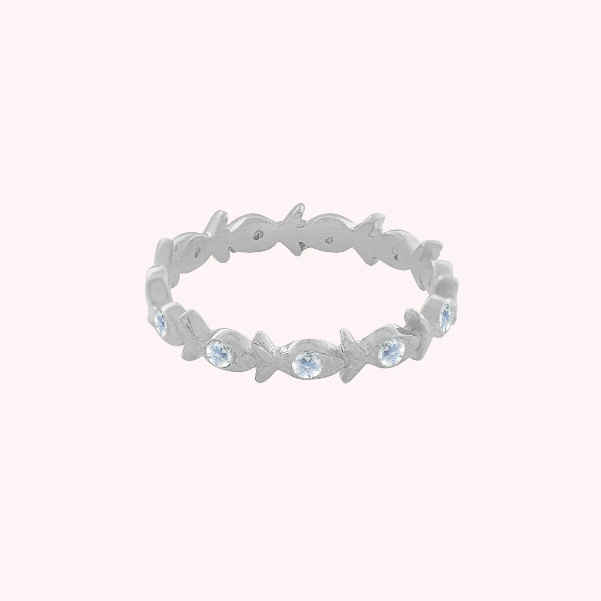 Fish_ring_sterling_silver_moonstone_eternity_band_in_front_angle_view_on_solid_pink_background