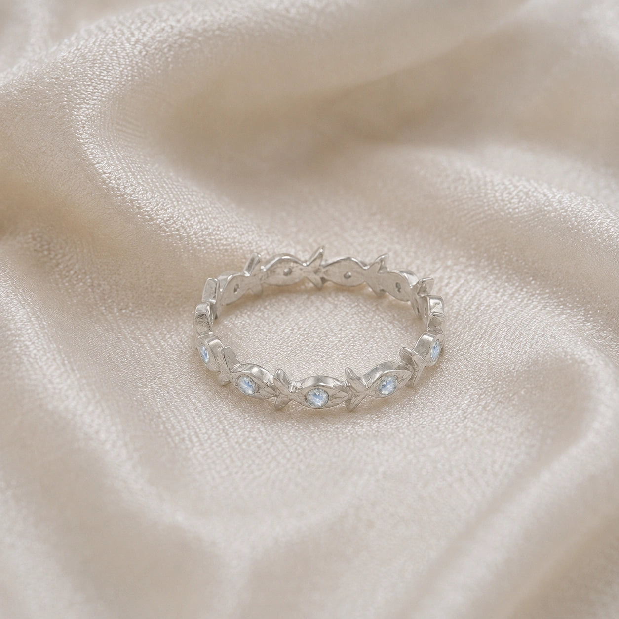 Fish_ring_sterling_silver_moonstone_eternity_band_in_front_angle_view_on_soft_fabric_background