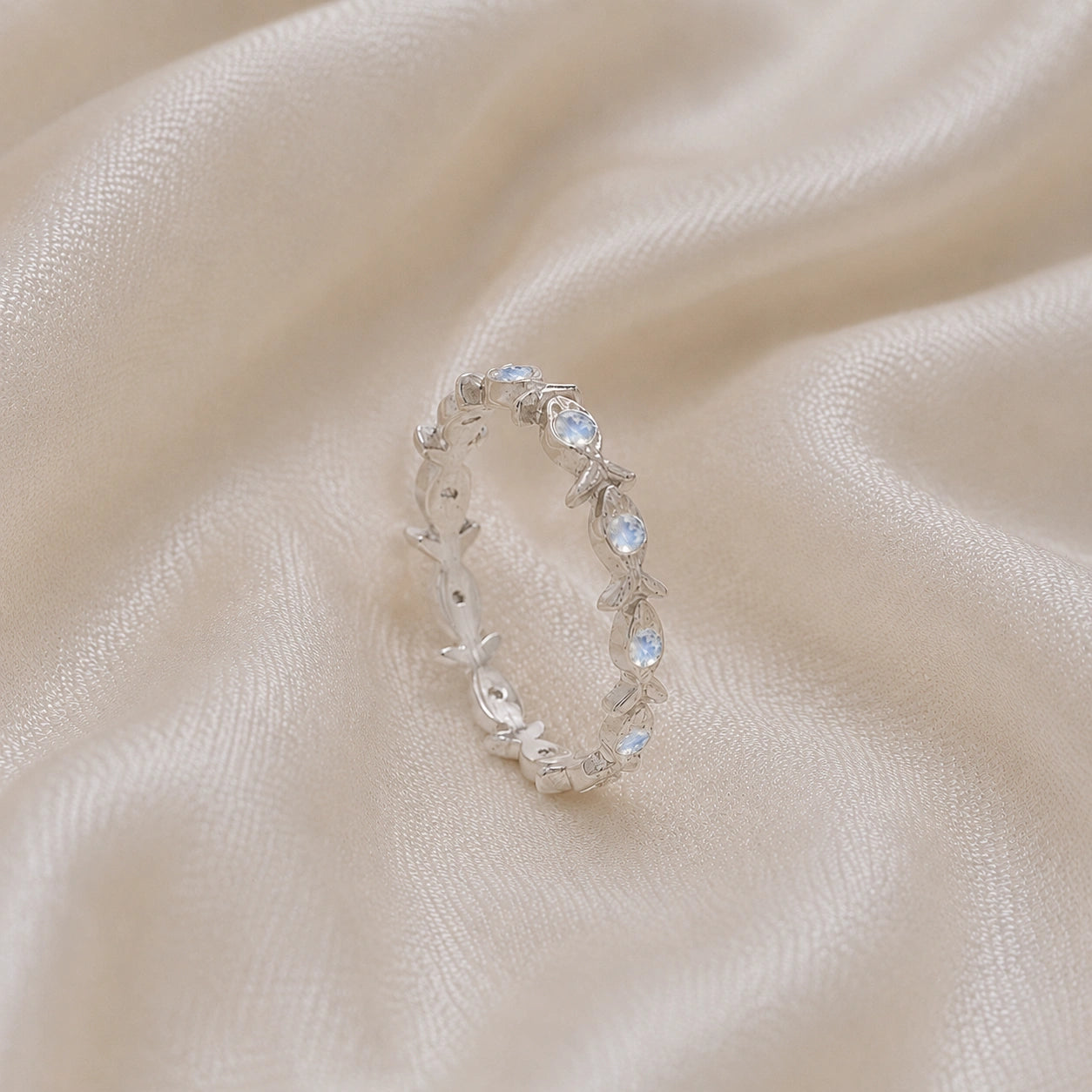 Fish_ring_sterling_silver_moonstone_eternity_band_in_side_angle_view_on_soft_fabric_background