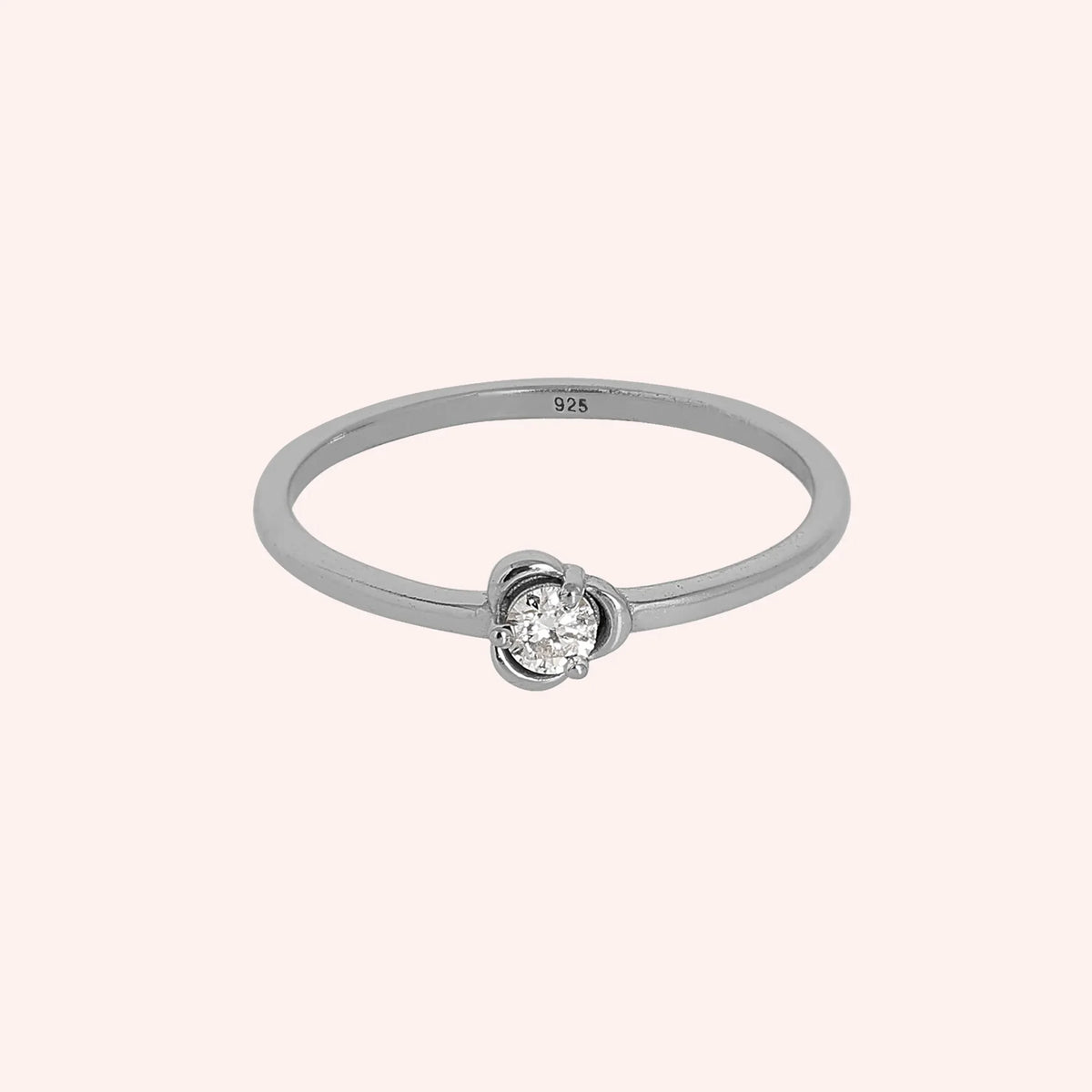 Flower_ring_in_sterling_silver_with_a_small_round_CZ_stone_at_front_angle_view_on_solid_pink_background