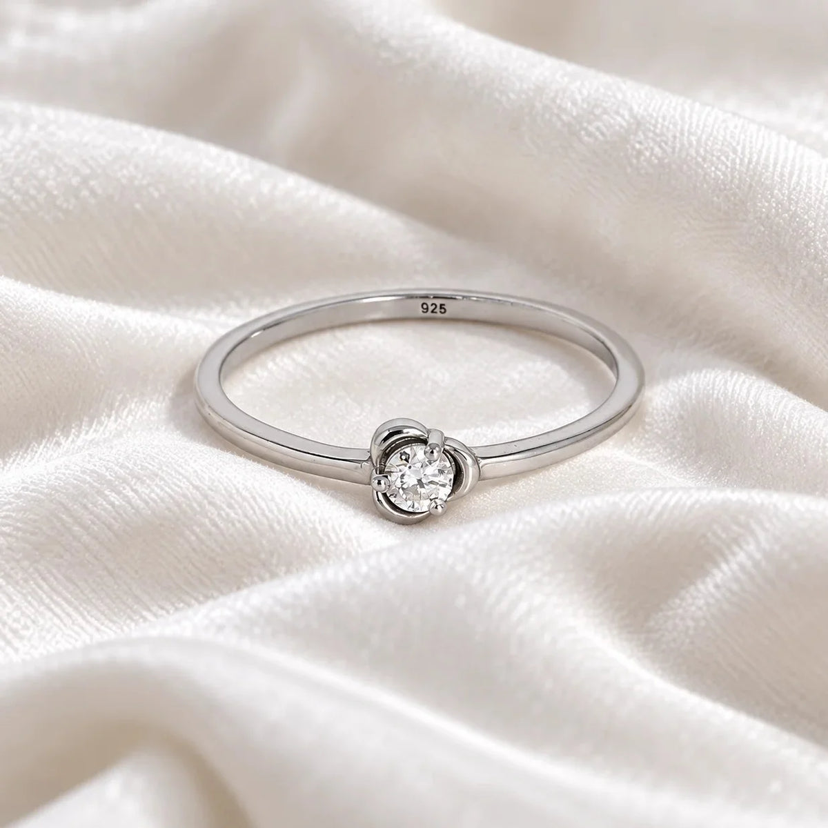 Flower_ring_in_sterling_silver_with_a_small_round_CZ_stone_at_front_angle_view_on_soft_fabric_background