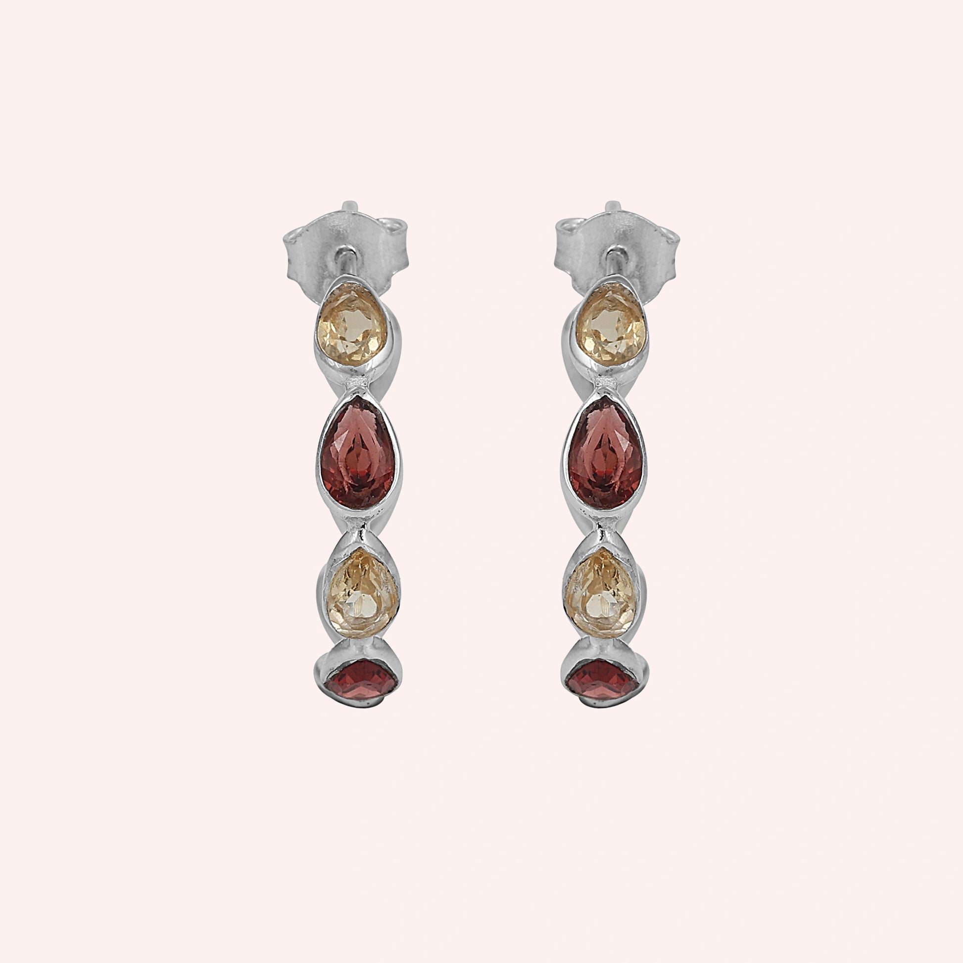 Silver hoop earrings featuring three pear cut citrine and two pear cut garnet stones on a pink background top down angle
